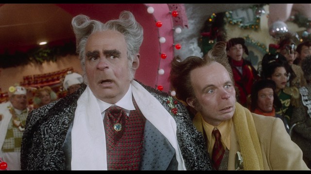 A scene from a movie featuring two young men sitting closely together in an airport waiting area, with one holding a box of popcorn.