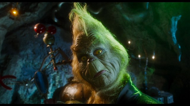 A man in a white suit and hat stands at a doorway, smiling, with a suburban landscape in the background.