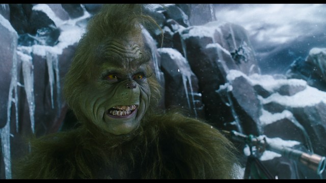 A close-up of a man with a concerned expression, with blurred figures in the background, set in a dimly lit interior.