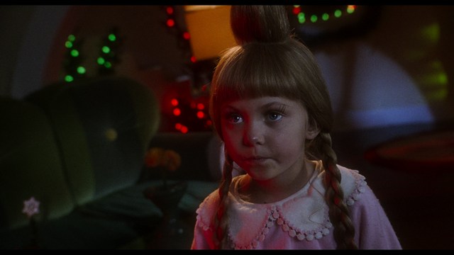 Two young men are looking at something off-camera, standing inside a building with bright lighting and seating areas visible in the background.