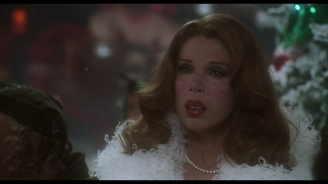 Close-up of a man with a serious expression, seated in a dimly lit area, with soft lighting from background lamps.