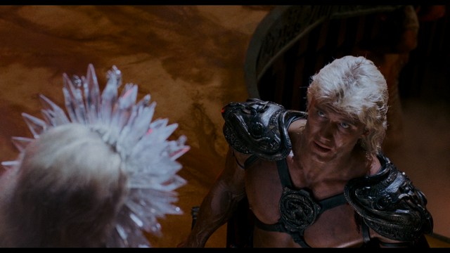 A scene from a movie featuring three characters standing on a bridge with a lush green landscape in the background.
