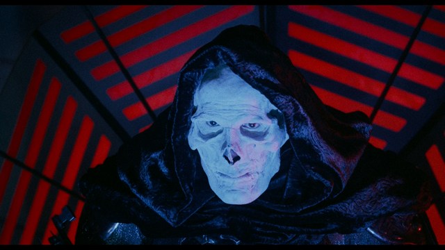 Scene featuring a character in a glowing white robe with long hair, standing in a futuristic environment at night with a city skyline in the background.