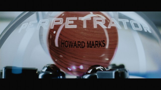A smiling man with a beard stands on a wooden boardwalk near the beach, with colorful flags in the background and a building visible in the distance.