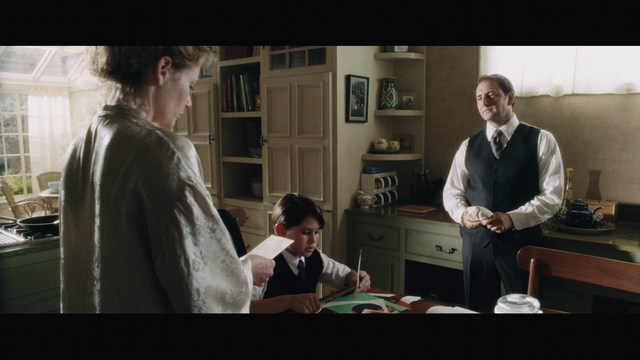 Scene from a church where a group of people, including a woman in a blazer and a young boy, are attending a service, facing forward with a stained glass window in the background.