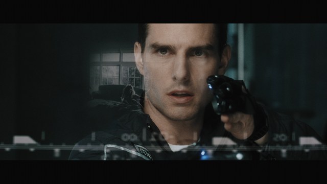 A woman with long dark hair resting her chin on her hand, looking pensively off to the side. In the background, various kitchen appliances and items are visible.