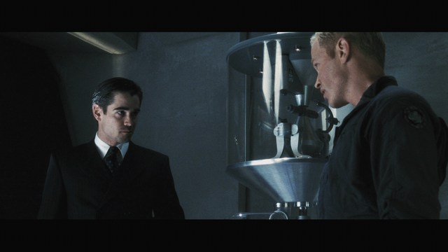 A man in a white suit and hat stands at the entrance of a house, smiling, with a suburban neighborhood visible in the background.