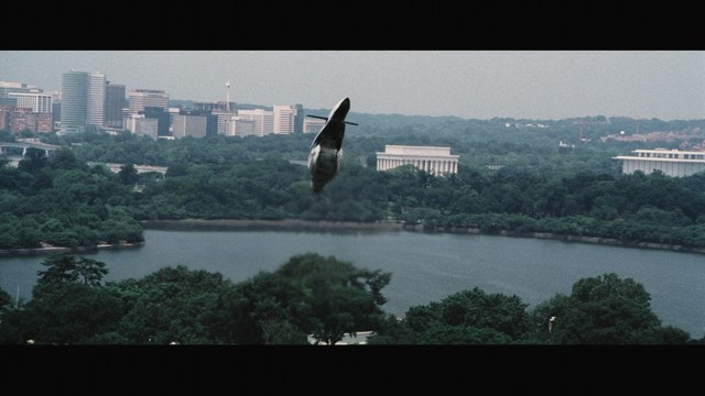 Two men sitting close together in a diner, one wearing a black beanie with the word 'SNOOGANS' and the other wearing a cap, both appearing engaged in conversation.
