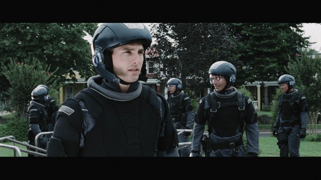 A close-up of a woman with dark hair and a serious expression sitting in a diner, with blurred background elements suggesting a busy atmosphere.