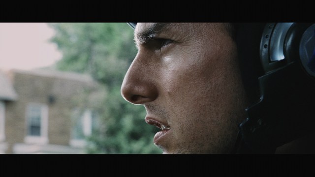 A young man aiming a handgun while seated, wearing a hoodie and looking tense.