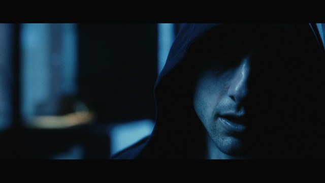 A woman with a shocked expression standing in the middle of a deserted road surrounded by lush greenery.