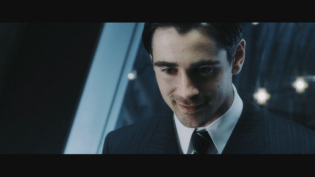 A bronze trophy figure of a cartoonish character with arms outstretched, positioned on a wooden table in a corporate setting, with a large window showcasing a mansion in the background.