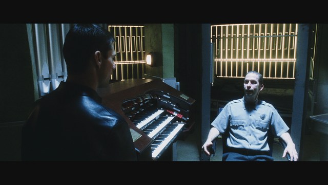 A man wearing a white suit and a fedora hat, looking surprised or upset, stands in a store with various products displayed in the background.