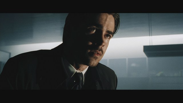 A man with dark hair and a hooded jacket smiles while sitting at a restaurant table, with blurred diners in the background.