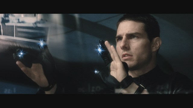 A close-up of a man wearing a red cardinal's hat and black clerical robes, seated in a leather armchair with a serious expression, in an office setting adorned with colorful posters.