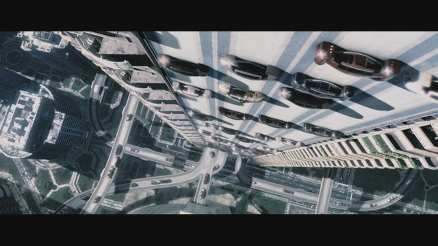 Aerial view looking down at a futuristic cityscape with cars driving on elevated roads beside tall buildings.