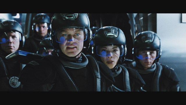 A group of armed personnel in futuristic uniforms looking intently at something off-screen, set against a dark, high-tech background.
