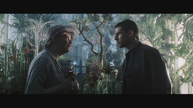 A scene from a film featuring two characters having a conversation in a greenhouse filled with various plants.