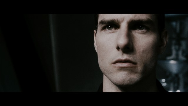 A serious-looking cardinal stands in front of a wooden backdrop with colorful posters related to Catholicism, holding a microphone at a press conference.