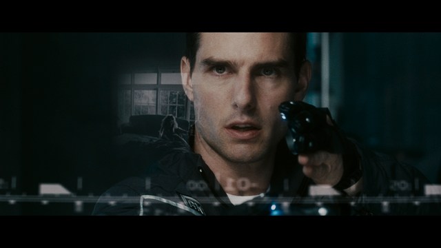 A woman with a pensive expression rests her chin on her hand, sitting at a table with kitchen appliances and items in the background.