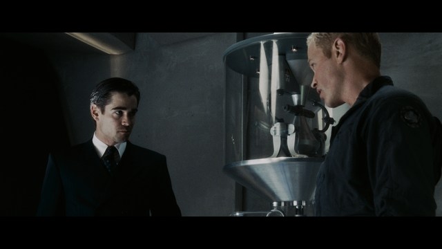 A man in a white suit and hat stands at a doorway, smiling, with a suburban landscape in the background.