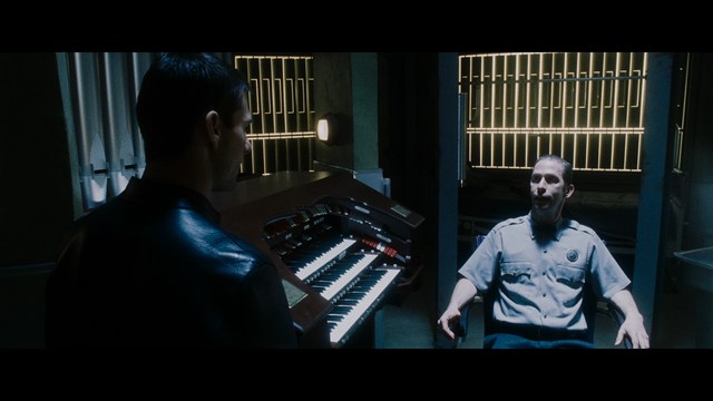 A close-up shot of a man wearing a white suit and a white hat, looking intently at someone in a retail store filled with merchandise.