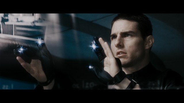 A serious-looking cardinal with a red hat and black robes sitting in a wooden chair in an office, surrounded by colorful posters and memorabilia.