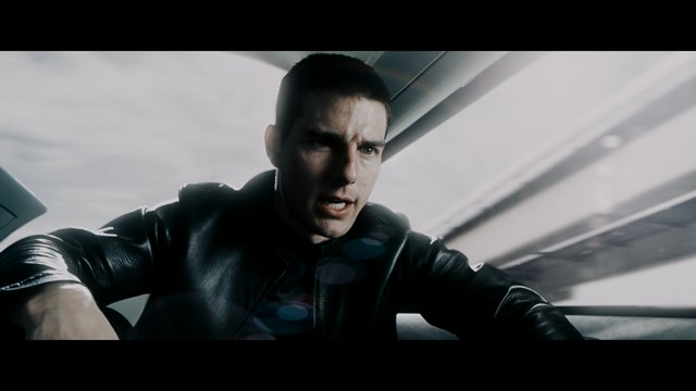 A tense scene featuring a woman with long hair and a serious expression, looking off to the side, while a man with short hair sits in the background, appearing relaxed and slightly turned away.