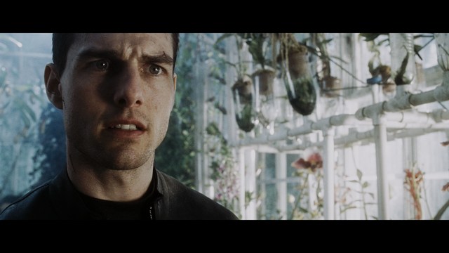 Close-up of a man with a concerned expression in a greenhouse setting, surrounded by various plants and soft lighting.