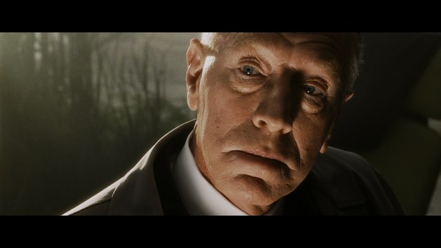 Close-up of a man with a concerned expression, wearing a suit, with a blurred background suggesting an indoor setting.