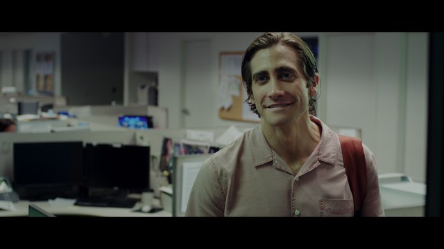 A group of people standing in a church, with a focus on a woman in a striped blazer looking up, while others are holding books or looking ahead.