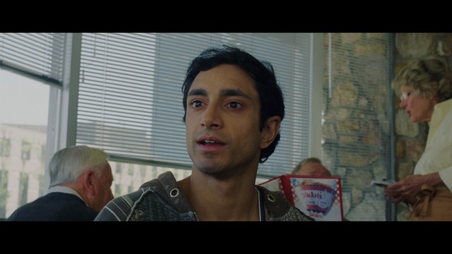 A close-up shot of a man with a distressed expression, featuring dark hair and wearing a blue hoodie, against a softly lit background.