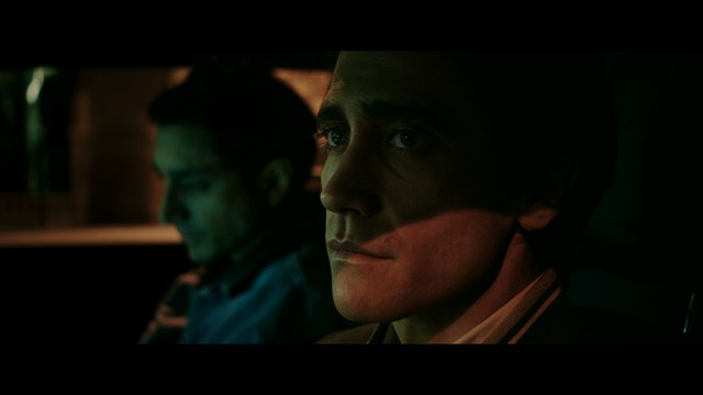 Close-up of a woman with long black hair sitting in a restaurant, looking concerned. A colorful painting is visible in the background, along with red bar stools.