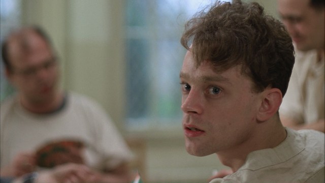 A scene featuring a man dressed as a cardinal, standing in front of a building with signs related to Catholicism.
