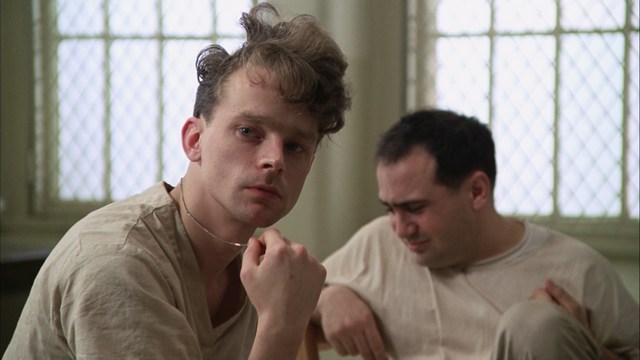 Scene from a church where a group of people, including a woman in a blazer and a young boy, are attending a service, facing forward with a stained glass window in the background.