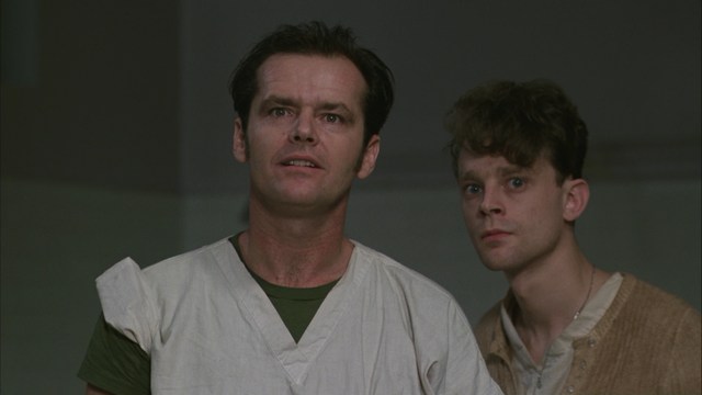 Scene featuring three characters on a roadside, discussing animatedly. A green landscape is visible in the background.