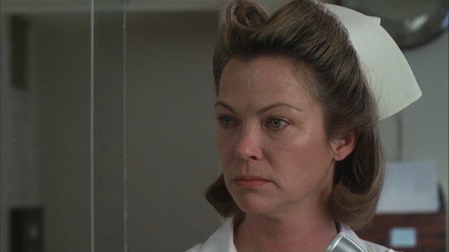 Two men engaged in conversation in a scene from a movie, set against a colorful playground background.