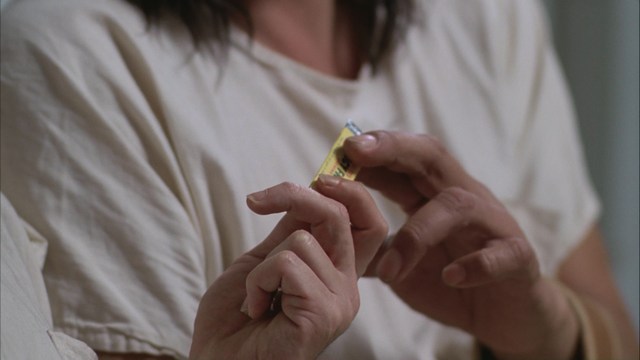 Two male characters in a movie scene, standing indoors near a doorway, with a blurred background of a waiting area.