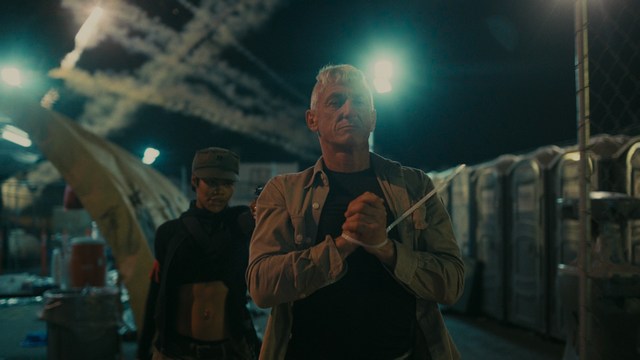 A scene from a movie featuring two young men sitting closely together in an airport waiting area, with one holding a box of popcorn.