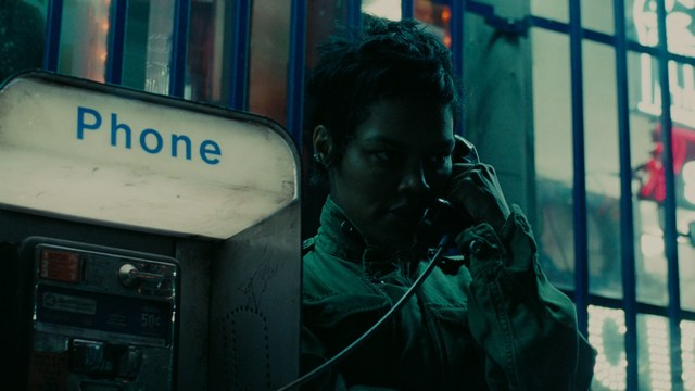 A group of people standing in a church, with a focus on a woman in a striped blazer looking up, while others are holding books or looking ahead.