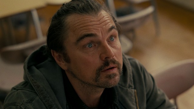 A close-up shot of a man with a distressed expression, featuring dark hair and wearing a blue hoodie, against a softly lit background.