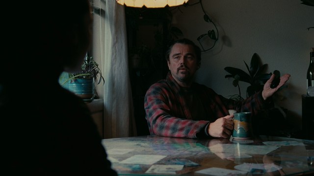 A woman with dark hair and a neutral expression sitting in a retro diner setting.