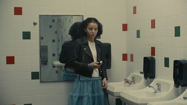 A scene from a movie featuring three characters standing on a bridge with a lush green landscape in the background.