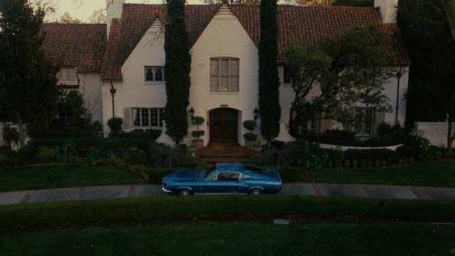 Two young men are looking at something off-camera, standing inside a building with bright lighting and seating areas visible in the background.