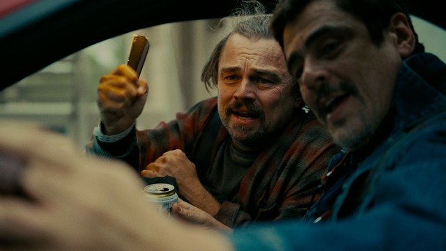 A man with dark, styled hair and a subtle smile seated at a restaurant table, with blurred diners in the background.