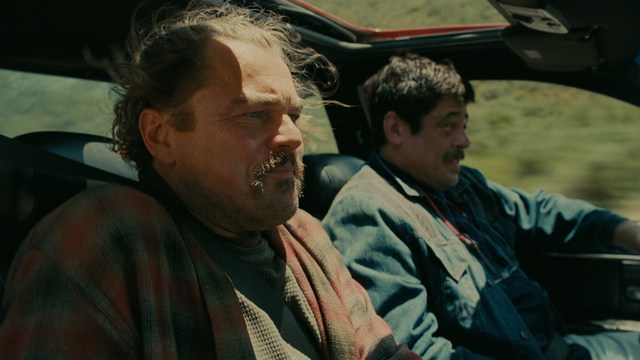 Two figures walking on a road towards a blue 'Welcome to New Jersey' sign.