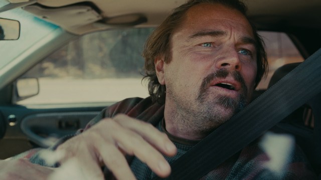A shocked man with long hair and a baseball cap sitting in a bar, looking surprised.