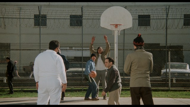 A scene featuring five characters in a bar setting, with a focus on their expressions and interactions. The backdrop includes bar shelves with bottles and a bartender visible in the background.