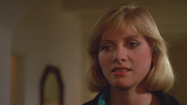 A young man aiming a handgun while seated, wearing a hoodie and looking tense.