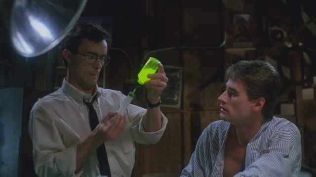 A man with short hair wearing a brown jacket and purple shirt, speaking animatedly in front of a colorful restaurant featuring a cartoon cow logo in the background.